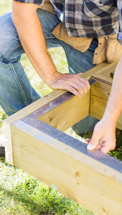 Handwerker misst rechtwinklig beim Bau eines Carports das Holz aus
